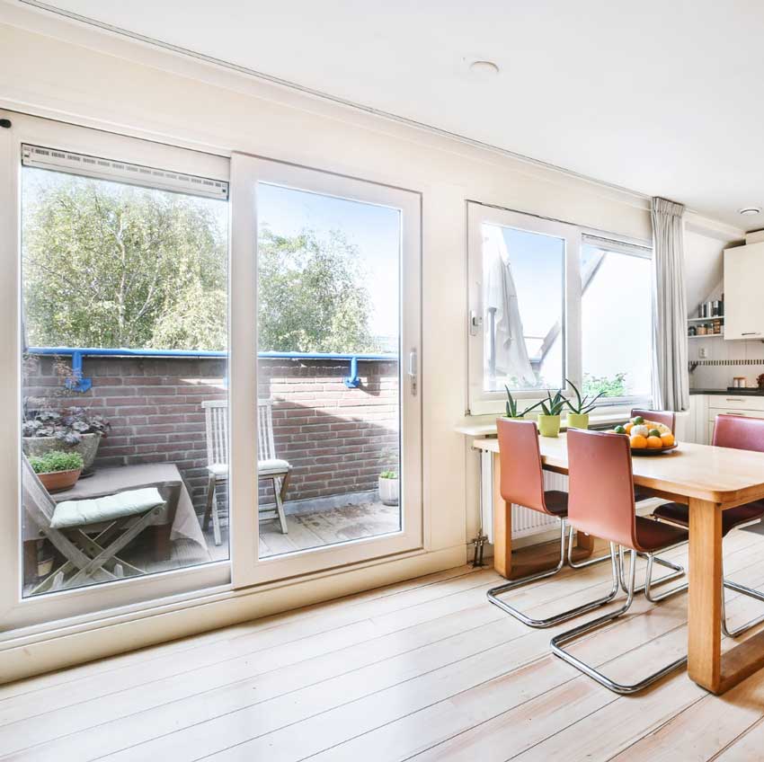 Couple sitting at a table by a large white-framed window enjoying coffee and conversation in a bright modern interior, highlighting natural light, comfort, and professional Window Replacement Atlanta services for stylish, energy-efficient spaces.