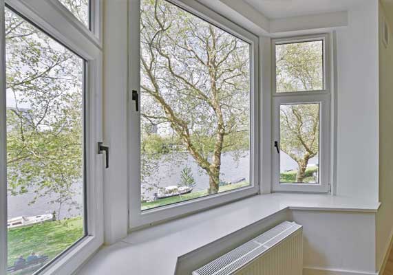 Interior view of white-framed windows overlooking trees and a river, filling the room with natural light and scenic views, showcasing modern design and professional Window Replacement Alpharetta services for improved comfort and efficiency.