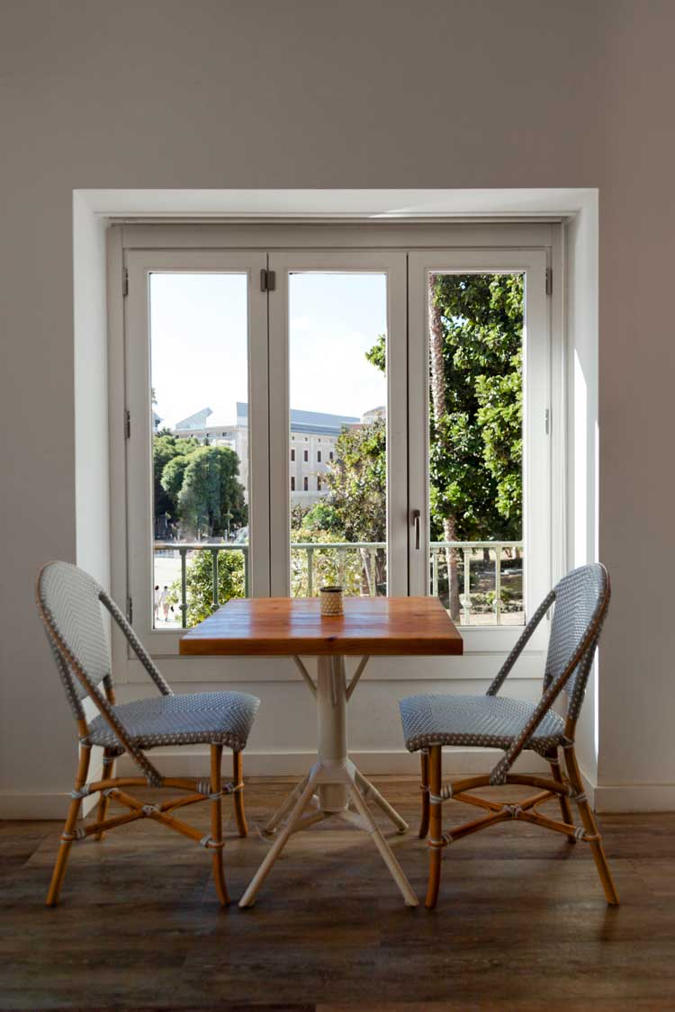 Cozy dining nook with a small table and chairs placed in front of large white-framed windows overlooking greenery and city buildings, highlighting natural light, comfort, and professional Window Replacement Alpharetta services for modern homes.