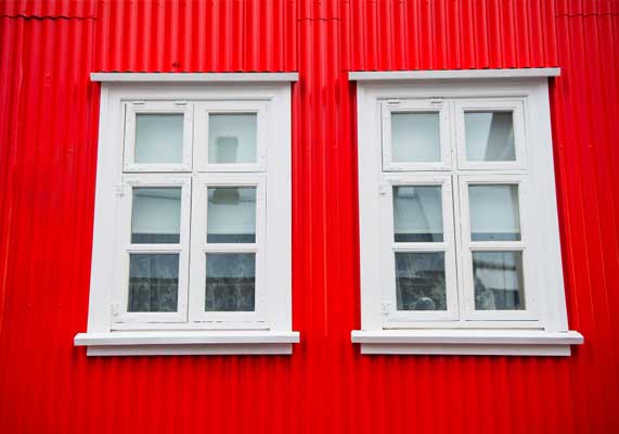 Red building exterior featuring two white-framed windows with classic grid design, creating strong visual contrast and showcasing durable materials with professional Window Replacement Atlanta services for improved efficiency and curb appeal.