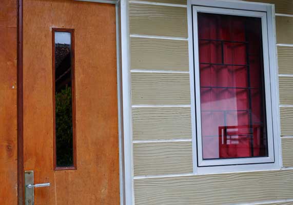 Home exterior featuring a white-framed window with red curtains next to a wooden entry door, showcasing clean siding, updated design, and professional Window Replacement Atlanta services for improved style and energy efficiency.