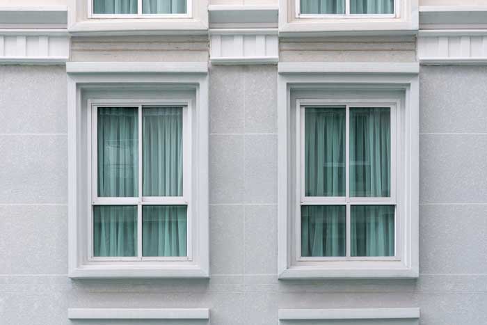 Building exterior featuring two white-framed double hung windows with curtains, showcasing classic architectural style, clean symmetry, and professionally installed Double Hung Windows Atlanta for durability and energy efficiency.