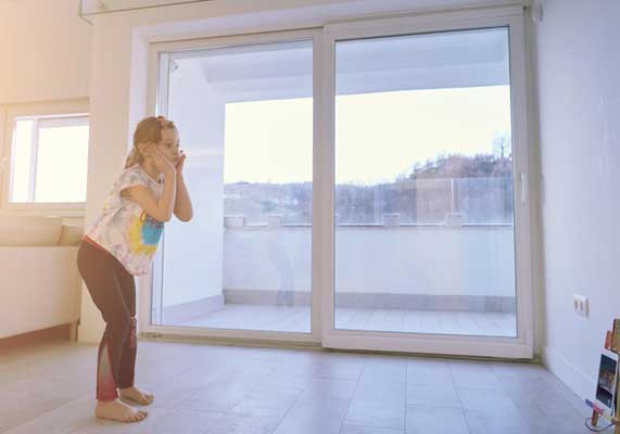 Child standing near large sliding glass windows in a bright modern room, enjoying natural light and outdoor views, highlighting safety, comfort, and professional Window Replacement Marietta services for family homes.