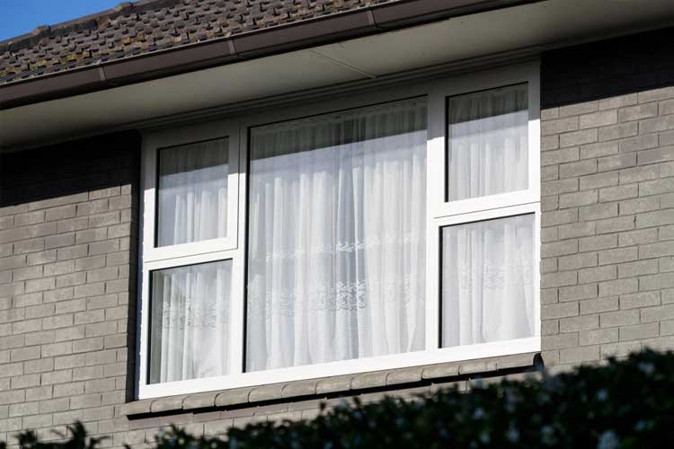 Exterior view of a residential home featuring large white-framed picture windows with curtains, enhancing natural light and curb appeal with Picture Windows Atlanta.