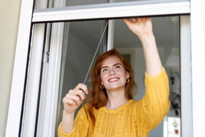 Smiling woman opening a modern sliding window inside a bright home, enjoying fresh air and natural light while highlighting smooth operation, comfort, and professionally installed Sliding Windows Atlanta.