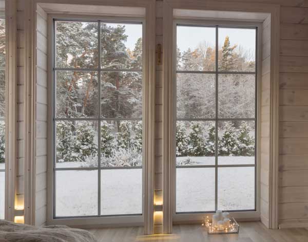 Interior view of double-pane windows with white frames overlooking a snowy winter landscape and trees, creating a cozy, light-filled room and showcasing energy-efficient New & Replacement Windows Atlanta for year-round comfort.