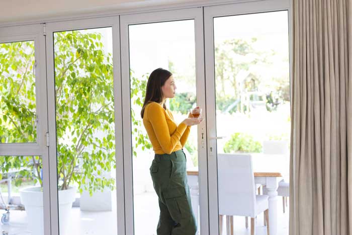 Woman standing by large glass patio doors holding a cup and enjoying natural light and garden views, highlighting modern home design, energy efficiency, and professionally installed New & Replacement Windows Atlanta.