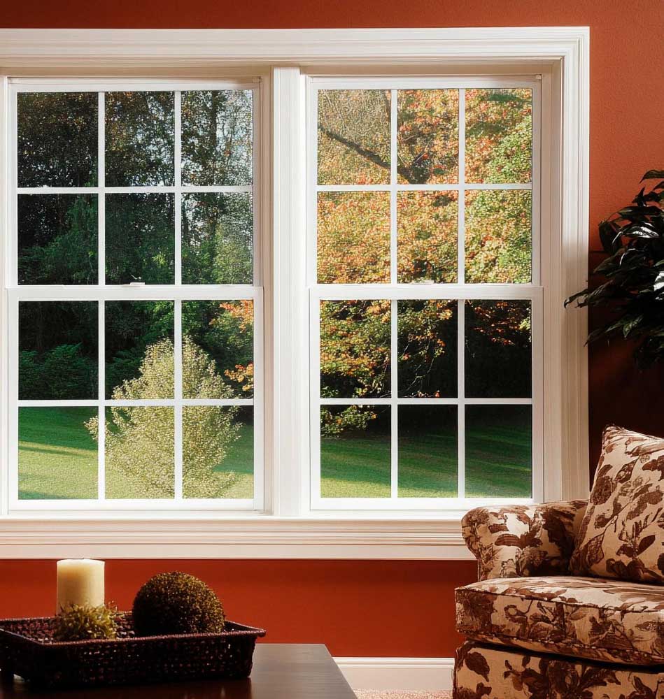 Window Replacement Woodstock featuring white double-hung grid windows in a cozy living room with an orange wall, offering a clear view of green trees outside and allowing abundant natural light into the home.